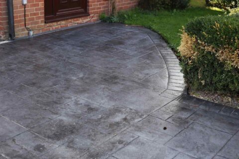 Imprinted concrete driveway with tile-pattern stamping curving toward a brick home's entry